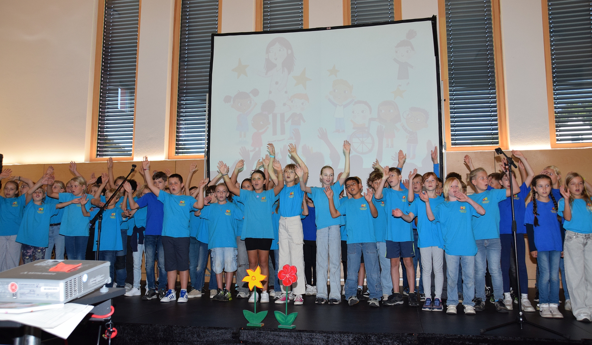 Foto mit Viertklässlern auf der Bühne, die Singen und ihre Arme schwenken